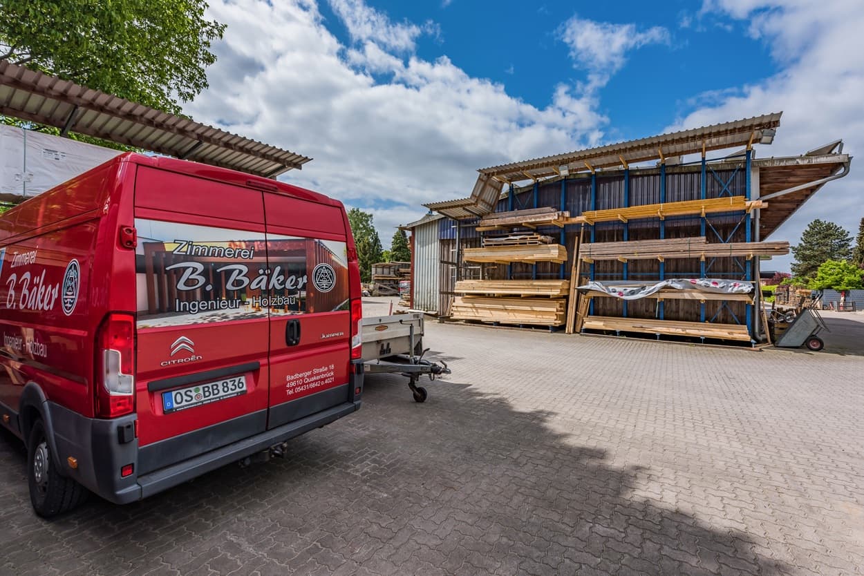 Holzmaterialien und Fahrzeug der Zimmerei Bäker im Hof.